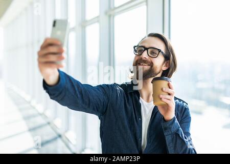 Porträt eines bärtigen Geschäftsmannes, der Hemd und Brille trägt, Videochats per Telefon während der Kaffeepause auf einer Treppe des Bürogebäudes Stockfoto