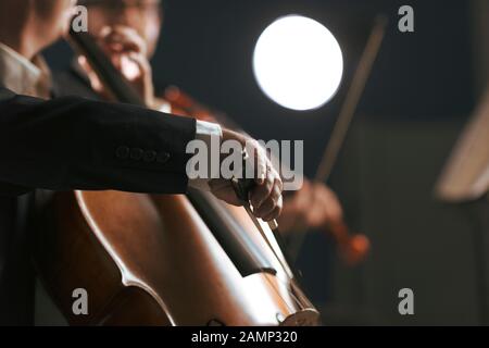 Sinfonisches Orchester, das auf der Bühne auftritt und ein klassisches Musikkonzert spielt, Cellist im Vordergrund, Hände nah dran Stockfoto