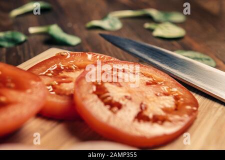 Nahaufnahme von Tomatenscheiben mit einem Messer auf einem Holzschneidebrett, veganer Nahrung und gesundem Lifestyle-Konzept Stockfoto