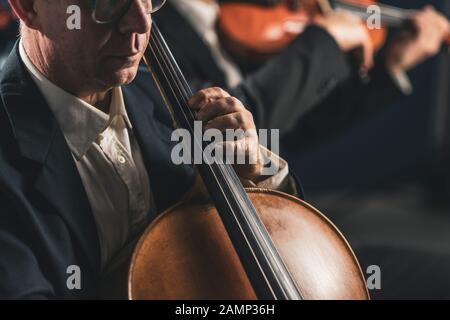 Sinfonisches Orchester, das auf der Bühne auftritt und ein klassisches Musikkonzert spielt, Cellist im Vordergrund, Hände nah dran Stockfoto