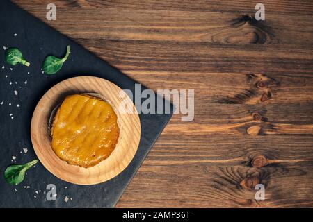 Draufsicht über einen veganen Burger mit geschmolzenem Käse auf einer Holzplatte in einem Schieferteller mit grünen Blättern, Holzhintergrund, veganer Nahrung und gesundem Lebensstil c Stockfoto