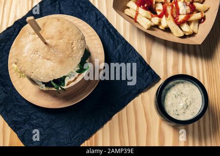 Draufsicht eines veganen Gourmet-Burgers auf einem Holztisch mit pommes frites mit Ketchup in einem Pappkarton und einem Mixbecher mit Sauce, gesundem Essen und Foodie Stockfoto
