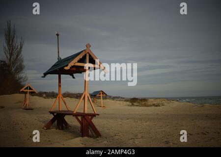 Sandiger Meeresstrand und alte Holzbänke mit blauen Dächern. Stockfoto