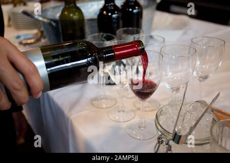 Nahaufnahme eines Kellners, der bei einem gesellschaftlichen Ereignis ein Glas Rotwein gießt. Stockfoto