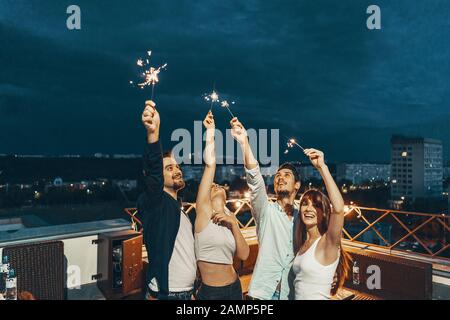 Freunde genießen eine Dachterrasse mit Party und Tanzen mit Wunderkerzen in den Händen Stockfoto