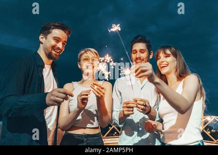 Freunde genießen eine Dachterrasse mit Party und Tanzen mit Wunderkerzen in den Händen Stockfoto