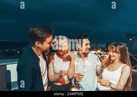 Freunde genießen eine Dachterrasse mit Party und Tanzen mit Wunderkerzen in den Händen Stockfoto