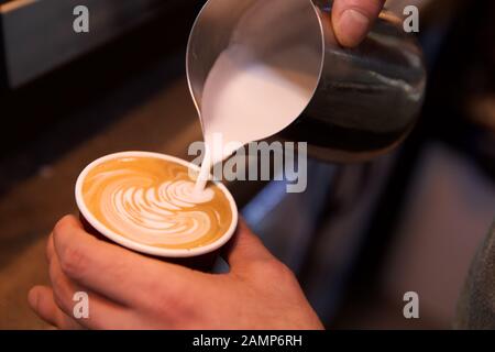 Nahaufnahme eines Barista, der einem Kaffee Schaummilch zufügt. Stockfoto