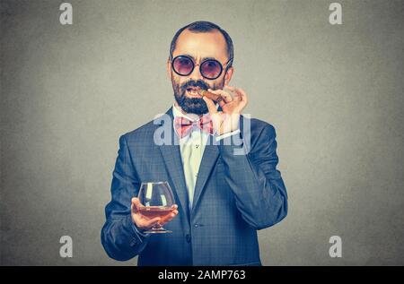 Wie ein Boss-Konzept. Nahaufnahme des Porträts eines selbstbewussten Geschäftsmannes, der eine kubanische Zigarre und ein Glas Wein mit Sonnenbrille raucht. Gemischte ra Stockfoto