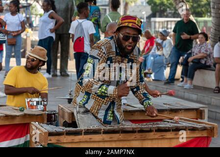 Kapstadt, Südafrika. Dezember 2019. Straßenmusiker in bunter Kleidung spielt Xylophon auf dem Hafengebiet der Innenstadt von Kapstadt. Stockfoto