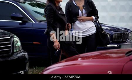 Zwei schlanke Frauen rauchen Zigaretten auf dem Parkplatz neben dem Club, Freundinnen brechen Stockfoto