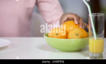 Weibliche Hand mit organischem Orange vom Teller, Körperpflege, frischem Saft auf dem Tisch Stockfoto