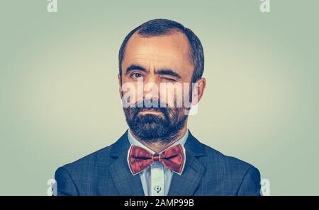 Nahaufnahme Porträt eines reifen Geschäftsmannes mit grauem Bart und Haarwinken, der Sie sicher auf Ihre Kamera blickt. Gemischtes Rennbären-Modell isoliert auf Green Ye Stockfoto