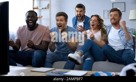 Multiethnische Gruppe von Freunden, die zu Hause Fußballspiele verfolgen und dabei das Ziel feiern Stockfoto