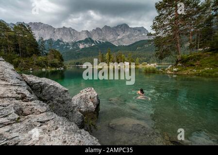 Frau schwimmt im See, Blick auf Eibsee vor Zugspitzmassiv mit Zugspitze, bewölkt, Wetterstein Range, bei Grainau, Oberbayern Stockfoto