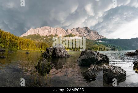 Felsen am Ufer, Eibsee vor Zugspitzmassiv mit Zugspitze, Sonnenuntergang, dramatische Mammaten-Wolken, Wetterstein Range, bei Grainau, oben Stockfoto