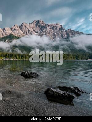 Felsen am Ufer, Eibsee vor Zugspitzmassiv mit Zugspitze, tief hängende Wolken, Wetterstein Range, bei Grainau, Oberbayern Stockfoto