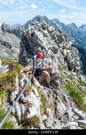 Lachende junge Frau mit Kletterhelm auf gesichertem Felsen, weibliche Klettererin auf einem Klettersteig, Mittenwald über Ferrata, Karwendelgebirge, Mittenwald Stockfoto