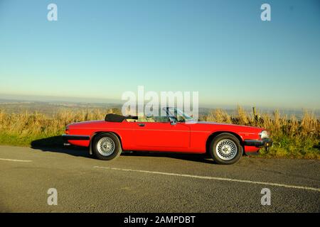 Ein rotes Jaguar XJS Cabriolet parkte an einem sonnigen Wintertag auf einer Landstraße Stockfoto