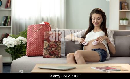 Zukünftige Mutter, die auf den Bauch niedliche, winzige Schuhe aufsetzt, Erwartung von Babymädchen, Einkaufen Stockfoto