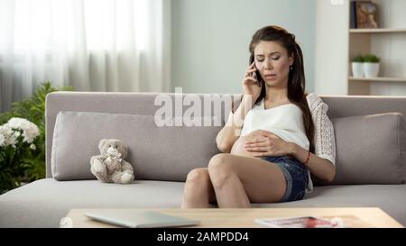 Unsichere schwangere Frau, die telefoniert, sich Sorgen um die Gesundheit macht und sich einsam fühlt Stockfoto