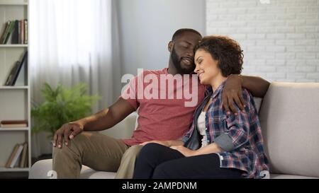 Zärtliche multirassische Paare umarmen sich, haben Ruhe im häuslichen Komfort, glückliche Heirat Stockfoto