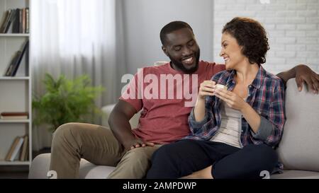 Glücklicher afroamerikanischer Mann, der seine glückliche Freundin mit Geschenk öffnet Stockfoto