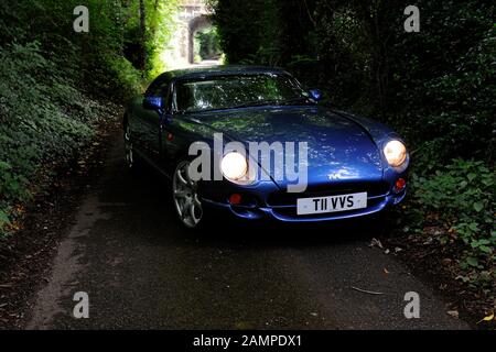 Der britische TVR Cerbera Muskelwagen parkte in einer dunklen und grünen Landspur mit eingeschalteten Scheinwerfern und einer dahinter liegenden Brücke Stockfoto