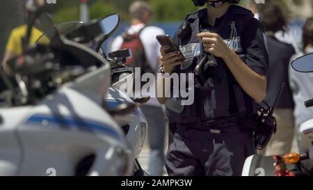 Polizistin steht neben dem Motorrad und überprüft das Handy im Dienst Stockfoto