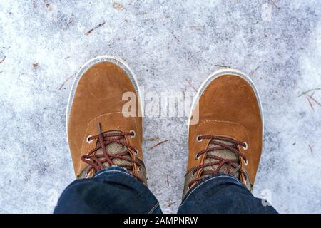 Zwei rote Stiefel auf den Füßen eines Mannes, der auf der eisigen Oberfläche des Sees steht. Stockfoto