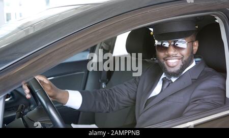 Schwarzer männlicher Fahrer sitzt im Auto und lächelt in die Kamera, Transportdienst Stockfoto