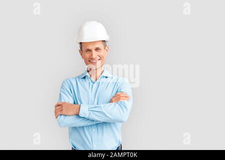 Konstruktion. Reifer Mann in Hardhut isoliert auf weißen gekreuzten Armen lächelnd verspielt Stockfoto