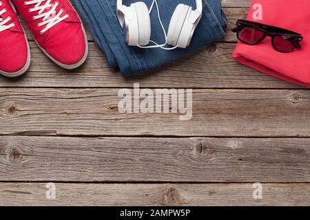 Kleidung und Accessoires. Turnschuhe, Jeans, Kopfhörer und Sonnenbrille. Urbanes Outfit für den Alltag oder Urlaub auf Holzhintergrund mit Kopiespac Stockfoto