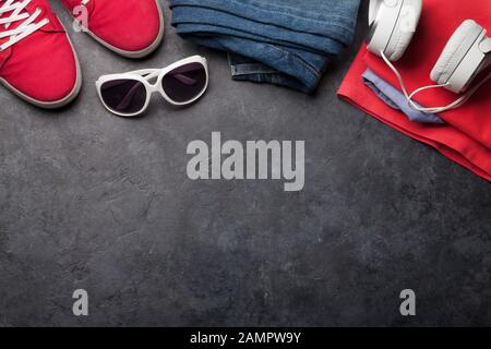 Kleidung und Accessoires. Turnschuhe, Jeans und Kopfhörer. Urbanes Outfit für den Alltag oder den Urlaub auf steinernem Hintergrund mit Platz für Kopien. Draufsicht f. Stockfoto