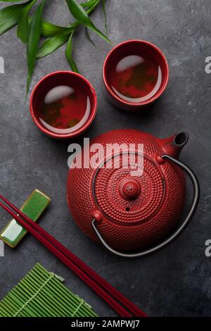 Grüner Tee in Schüsseln und Teekanne und Sushi-Essstäbchen auf Steintisch. Draufsicht Stockfoto