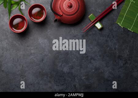 Grüner Tee in Schüsseln und Teekanne und Sushi-Essstäbchen auf Steintisch. Draufsicht mit Kopierbereich Stockfoto