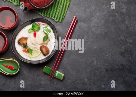 Tom Kha traditionelle thailändische Suppe mit Huhn, Pilzen, Kokosmilch und heißen Gewürzen. Mit grünem Tee in Topf und Schüsseln. Draufsicht mit Kopierbereich Stockfoto