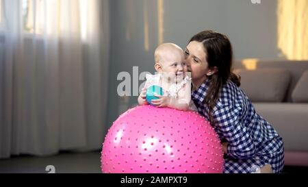 Fröhliche Mutter, die mit Kleinkind spielt und Baby-Fitnessübungen auf dem großen Ball macht Stockfoto