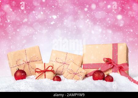 Weihnachtsgeschenke in braunem Papier mit rotem Band auf pinkfarbenem, schneebedeckten Hintergrund verpackt Stockfoto
