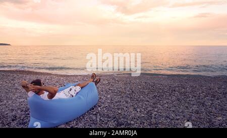 Freier Mann, der sich am Strand entspannt, mit Blick auf die Küste genießt und sich im Urlaub ausruhen kann Stockfoto