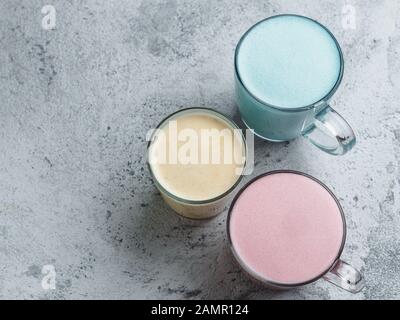 Trendgetränke: Blau, Gelb und Pink latte. Blick von oben auf die heiße Butterfly pea oder Blue spirulina Latte, Gelb oder Gold Gelbwurz latte und Rosa rote Beete latte auf grauem Zement Hintergrund. Kopieren Sie Platz für Text Stockfoto