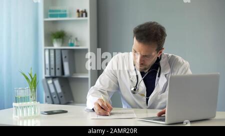 Arzt, der die Testergebnisse auf dem Laptop betrachtet und medizinische Aufzeichnungen, Medikamente aufschreibt Stockfoto