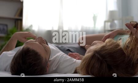 Glückliches junges Paar liegt im Bett, lacht und genießt Zeit, zärtliche Beziehungen Stockfoto