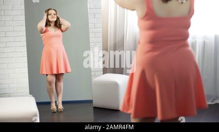 Fröhliche, fette Frau im Kleid, die ihre Spiegelreflexion bewundert und genießt es, zupft zu werden Stockfoto