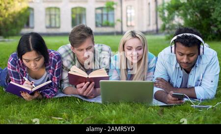 Multiethnische Männer und Frauen machen Hausaufgaben auf dem Rasen auf dem Campus, Hochschulbildung Stockfoto