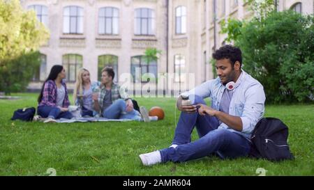 Hispanischer Student sitzt auf Gras und benutzt Handy, App für Bekannte Stockfoto