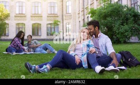 Multiracial Paare, die sich auf Gras entspannen, umarmen und lächeln, erste Liebe, Studenten Stockfoto