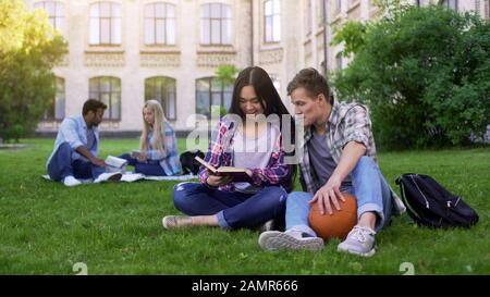 Studenten-Paar sitzt auf dem Rasen auf dem Campus, studiert und bereitet sich auf den Abschlusstest vor Stockfoto