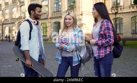 Fröhliche hispanische Männer, die mit Mädchen in der Nähe des College sprechen, Pause, Freundschaft Stockfoto