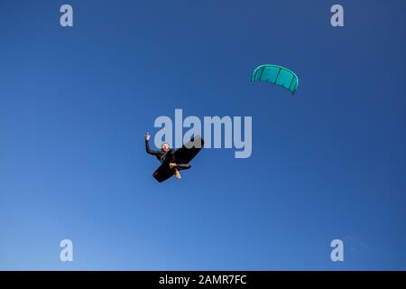 Kite Surfer rodeo Stil auf seinem Brett in der Luft mit der Hand Geste in die Luft. Stockfoto